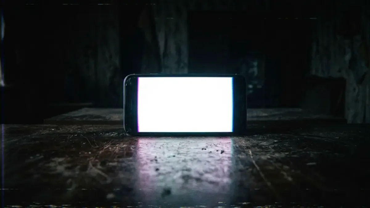 Teléfono celular boca arriba sobre una mesa oscura con la pantalla encendida en blanco